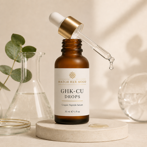 An amber glass dropper bottle labeled 'MATCH HER MOOD GHK-CU DROPS' sits on a round stone pedestal with a glass dropper resting above it. The bottle is styled with a small glass beaker and eucalyptus leaves in a warm, softly lit setting.